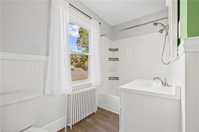 bathroom featuring radiator, tub / shower combination, toilet, wood finished floors, and a sink
