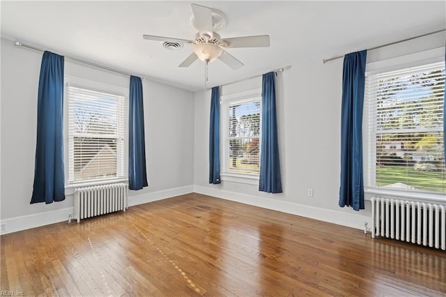 empty room with radiator heating unit, a wealth of natural light, and wood finished floors