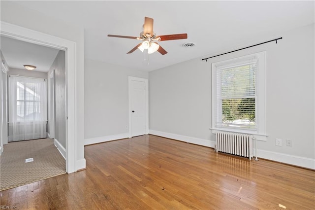 unfurnished room featuring baseboards, a ceiling fan, visible vents, radiator, and wood finished floors