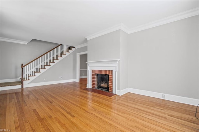 unfurnished living room with baseboards, a fireplace, crown molding, stairs, and wood finished floors