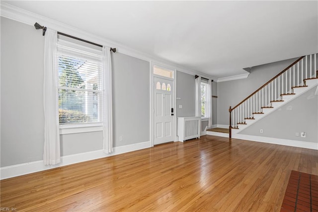 foyer with light wood finished floors, crown molding, radiator heating unit, and stairs