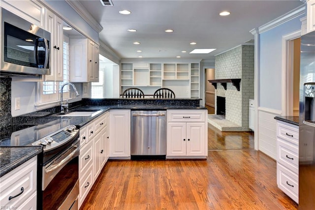 kitchen with crown molding, a peninsula, white cabinets, a sink, and stainless steel appliances