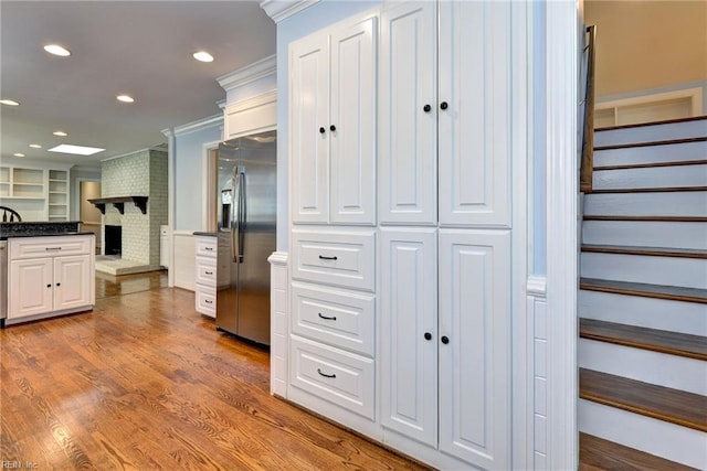 kitchen featuring a fireplace, white cabinetry, built in fridge, crown molding, and wood finished floors