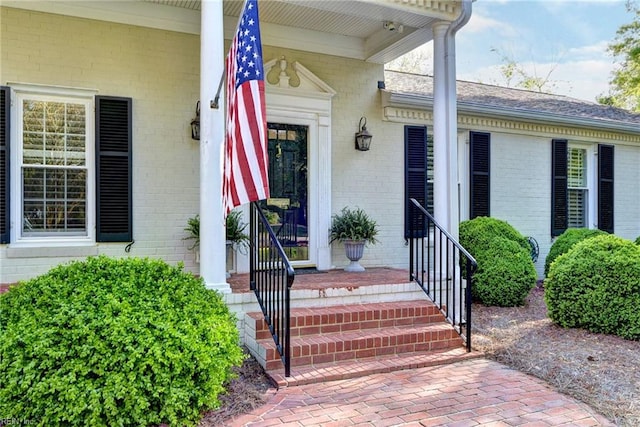 entrance to property featuring brick siding and a shingled roof