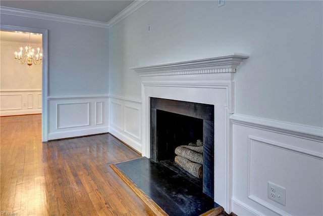interior details with a chandelier, wood finished floors, ornamental molding, and a wainscoted wall