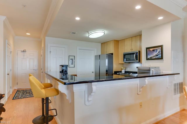 kitchen featuring dark countertops, a kitchen breakfast bar, stainless steel appliances, light wood-style flooring, and baseboards