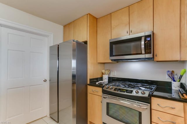 kitchen with dark countertops, light brown cabinetry, stainless steel appliances, and light tile patterned flooring