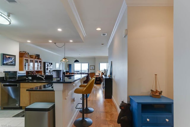 kitchen featuring ornamental molding, stainless steel dishwasher, dark countertops, and a breakfast bar