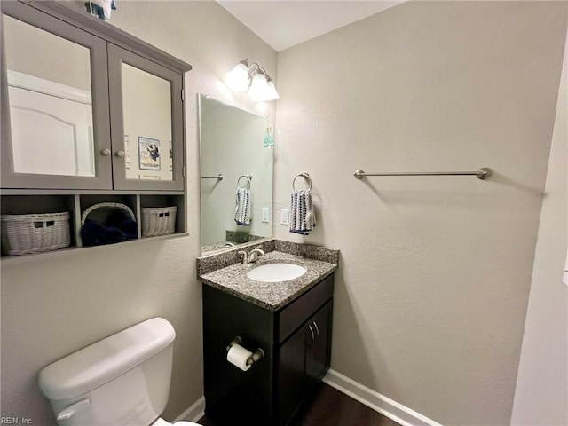 half bathroom with toilet, wood finished floors, vanity, and baseboards