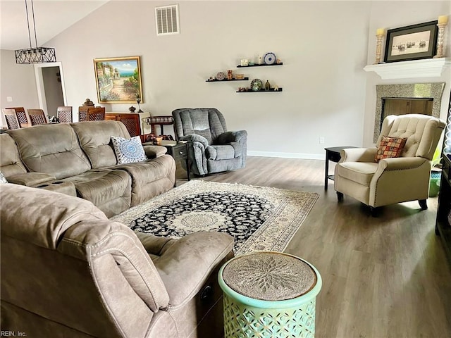 living area with a fireplace, vaulted ceiling, visible vents, wood finished floors, and baseboards
