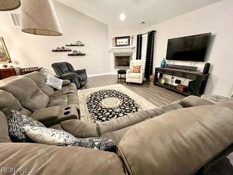 living area with baseboards, a fireplace, visible vents, lofted ceiling, and wood finished floors