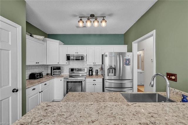 kitchen featuring a sink, decorative backsplash, appliances with stainless steel finishes, and white cabinetry