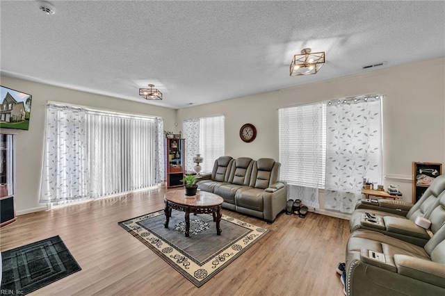 living room with visible vents, a textured ceiling, baseboards, and wood finished floors