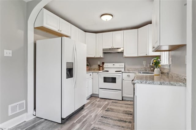 kitchen with white appliances, under cabinet range hood, light wood-style floors, visible vents, and a sink