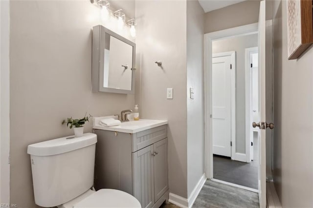 half bathroom featuring toilet, vanity, wood finished floors, and baseboards