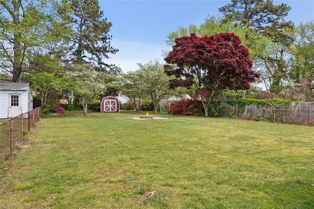 view of yard featuring a fire pit, a fenced backyard, an outdoor structure, and a storage unit
