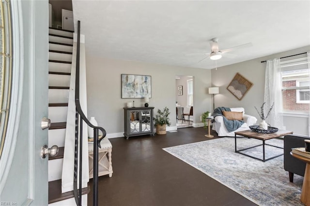 living area with ceiling fan, stairway, and baseboards
