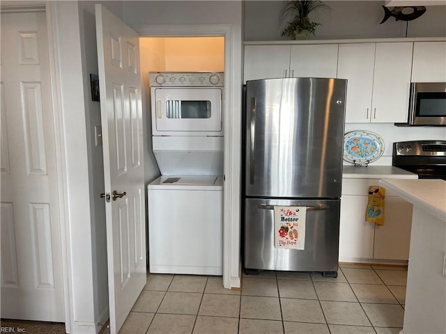 kitchen featuring white cabinets, stacked washer and clothes dryer, light tile patterned floors, and stainless steel appliances