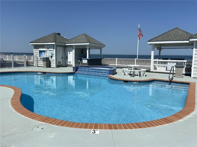 view of pool featuring a patio, a pool with connected hot tub, a water view, a gazebo, and fence