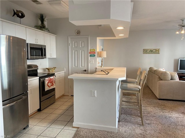 kitchen with light tile patterned floors, open floor plan, light countertops, appliances with stainless steel finishes, and a kitchen bar