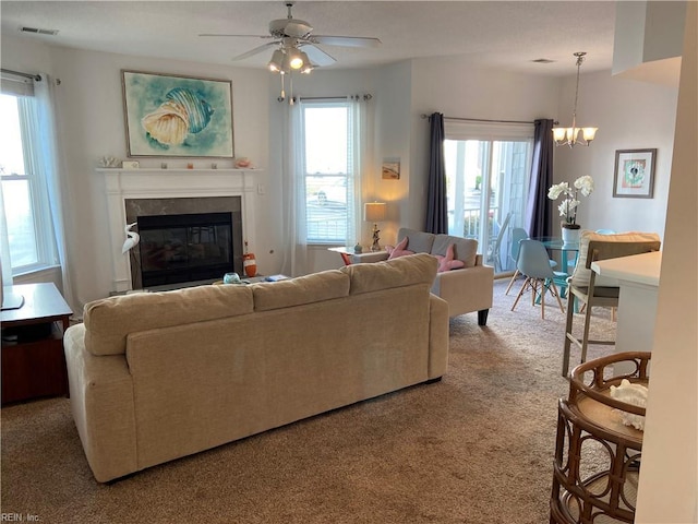 carpeted living room with visible vents, a healthy amount of sunlight, a glass covered fireplace, and ceiling fan with notable chandelier