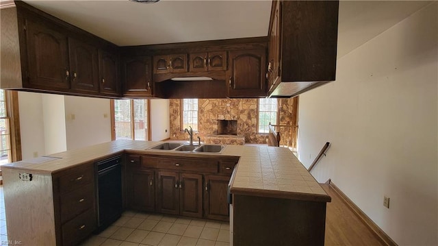 kitchen featuring tile countertops, a peninsula, dark brown cabinets, black dishwasher, and a sink