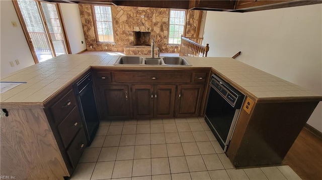 kitchen with a sink, tile counters, open floor plan, and black dishwasher