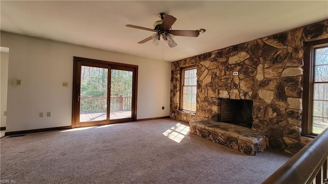 unfurnished living room featuring carpet flooring, a stone fireplace, baseboards, and a ceiling fan