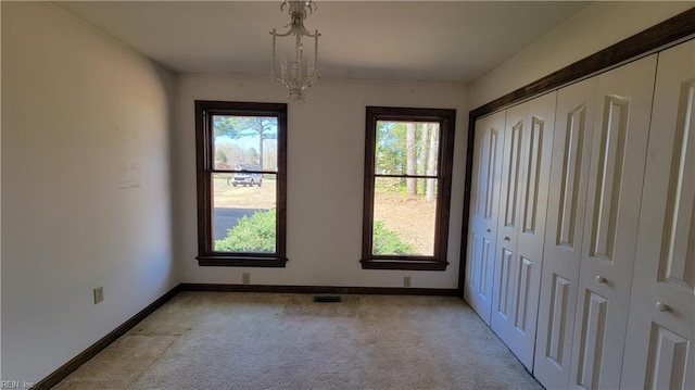 unfurnished bedroom featuring a chandelier, light carpet, a closet, and baseboards