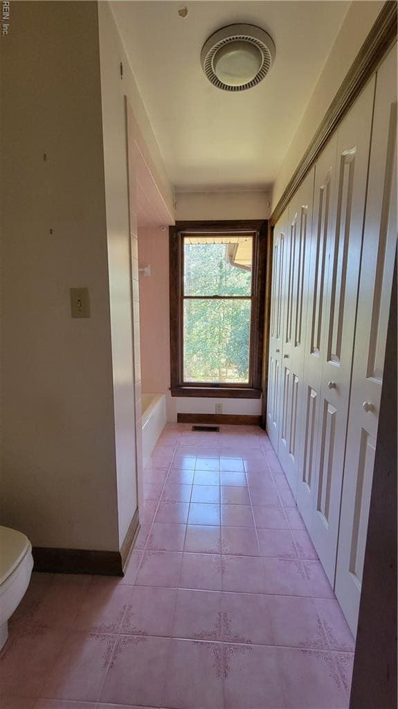hallway with light tile patterned floors, baseboards, and visible vents