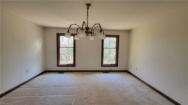 carpeted spare room featuring visible vents, a notable chandelier, and baseboards