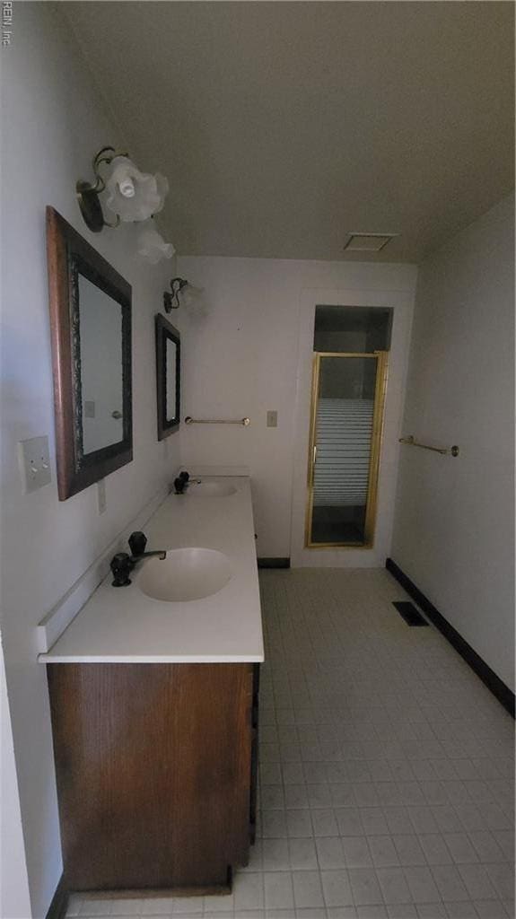 bathroom featuring baseboards, double vanity, a shower stall, visible vents, and a sink