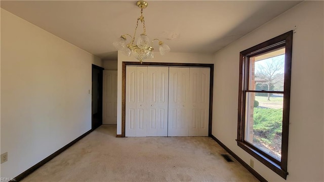 unfurnished bedroom featuring light colored carpet, a notable chandelier, multiple windows, and visible vents