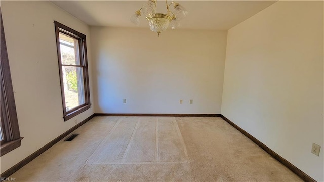 empty room featuring a notable chandelier, visible vents, light colored carpet, and baseboards