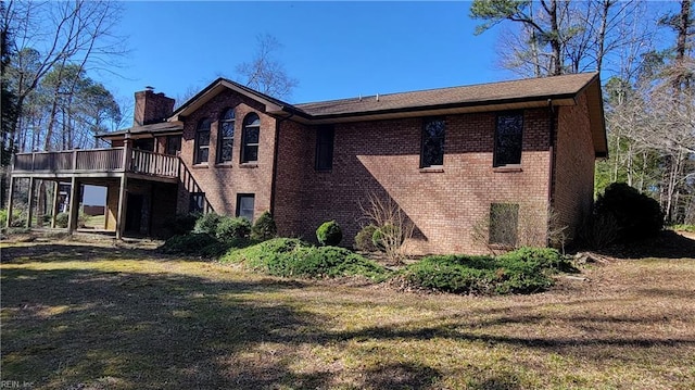 view of side of property featuring brick siding, a deck, a yard, and a chimney