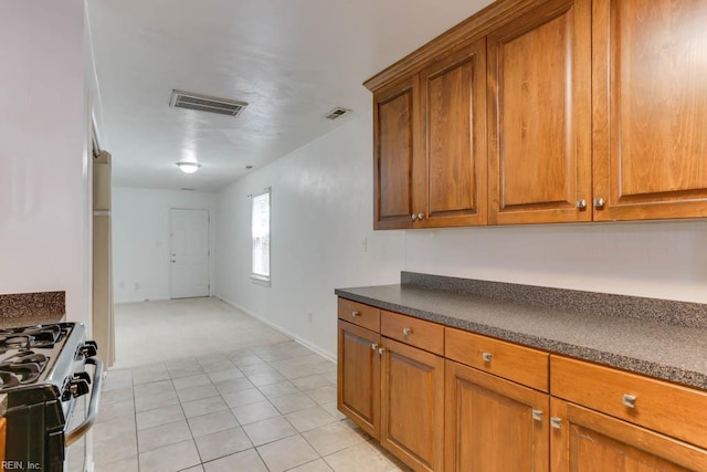 kitchen with brown cabinetry, stainless steel gas range, dark countertops, and visible vents
