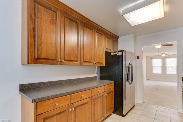 kitchen featuring stainless steel fridge with ice dispenser, light tile patterned floors, a ceiling fan, dark countertops, and brown cabinets