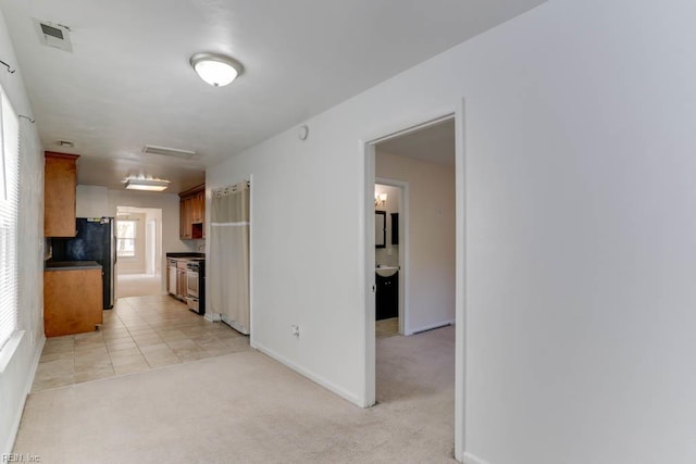 interior space featuring freestanding refrigerator, visible vents, light carpet, brown cabinets, and baseboards
