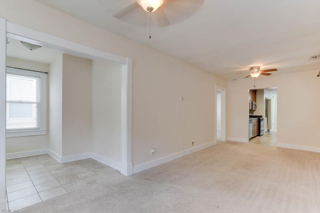 spare room featuring light carpet, ceiling fan, and baseboards