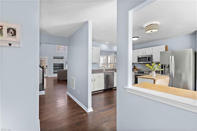 kitchen with decorative backsplash, white cabinets, baseboards, appliances with stainless steel finishes, and dark wood-style floors