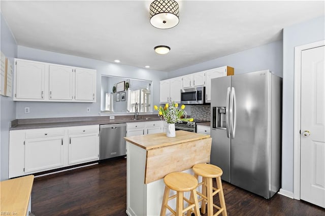 kitchen featuring white cabinets, a breakfast bar area, appliances with stainless steel finishes, and dark wood-style flooring
