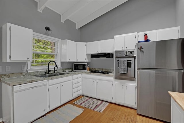 kitchen with light wood finished floors, stainless steel appliances, a sink, high vaulted ceiling, and white cabinetry