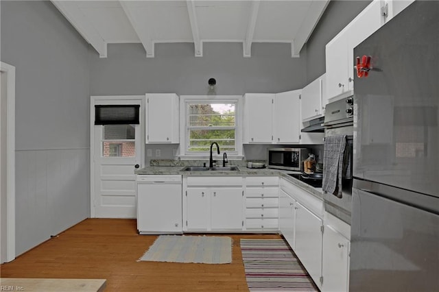 kitchen with beamed ceiling, stainless steel appliances, white cabinets, and a sink