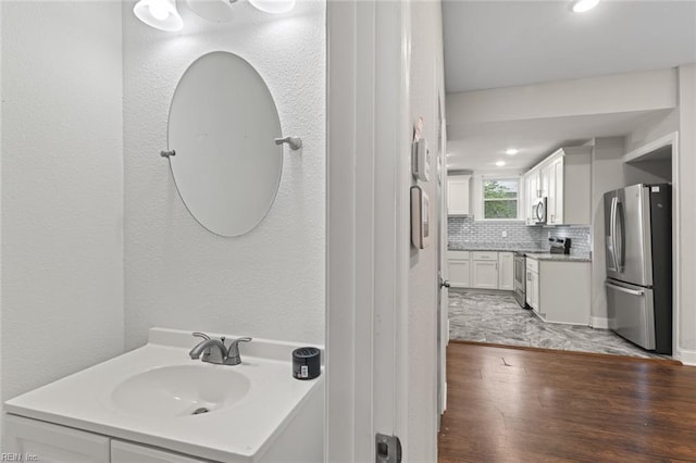 bathroom featuring decorative backsplash, a textured wall, recessed lighting, wood finished floors, and vanity