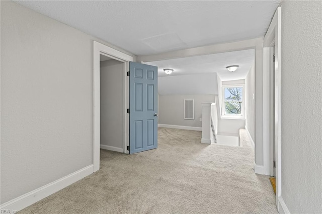 hallway featuring an upstairs landing, carpet, visible vents, and a textured wall