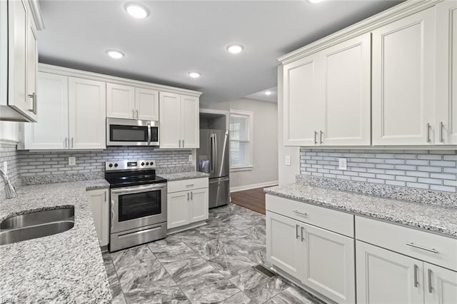 kitchen featuring a sink, tasteful backsplash, white cabinetry, baseboards, and appliances with stainless steel finishes