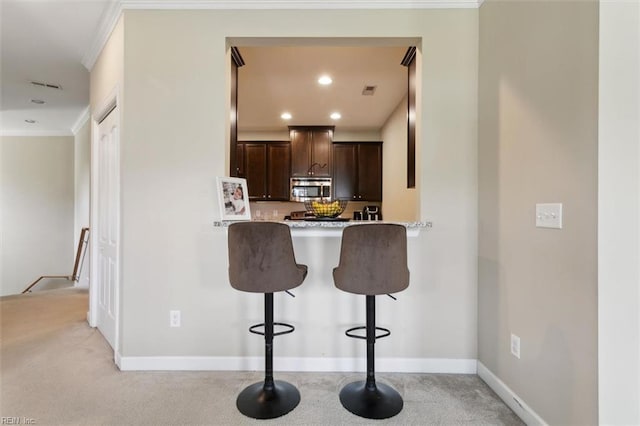 kitchen featuring ornamental molding, light countertops, a kitchen breakfast bar, dark brown cabinetry, and stainless steel microwave