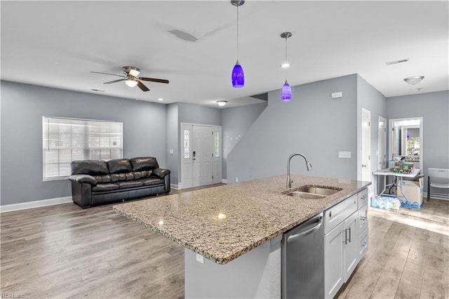 kitchen with stainless steel dishwasher, light stone countertops, light wood-type flooring, white cabinetry, and a sink