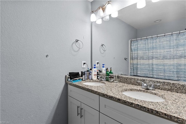 full bathroom with double vanity, a textured wall, and a sink