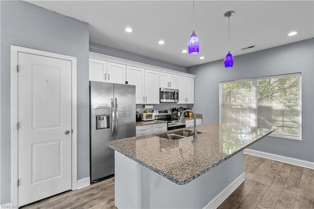 kitchen featuring an island with sink, white cabinetry, stainless steel appliances, a sink, and wood finished floors